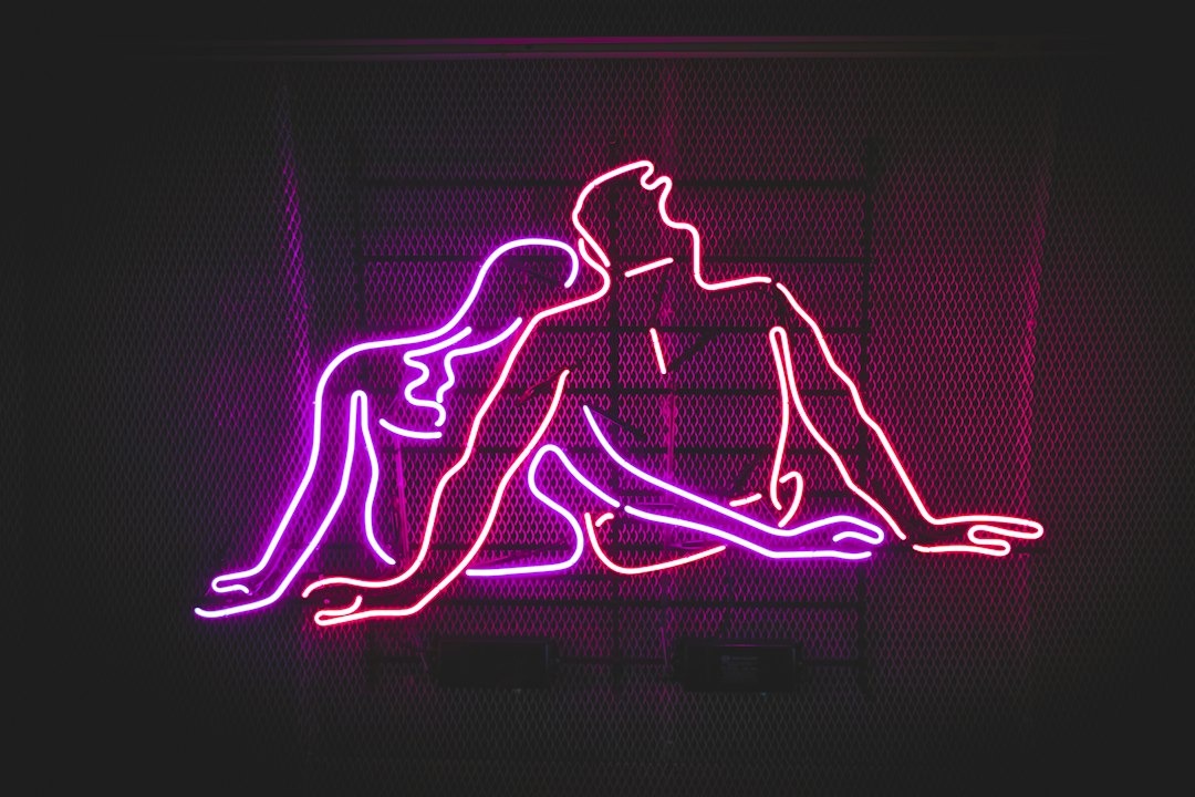 Neon light figures leaning into each other on a metal grid.
